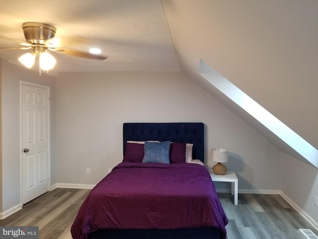 bedroom with visible vents, wood finished floors, vaulted ceiling with skylight, baseboards, and ceiling fan