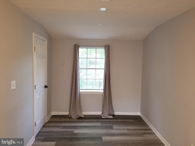 empty room featuring baseboards, dark wood-style flooring, and vaulted ceiling