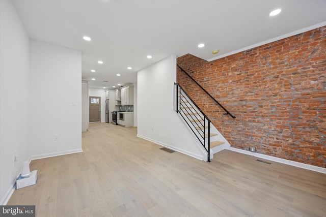 unfurnished living room with light wood-style flooring, visible vents, and brick wall