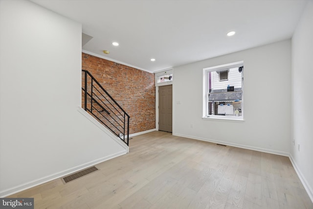 foyer entrance with baseboards, visible vents, brick wall, light wood-style flooring, and stairs