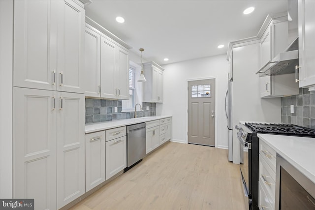 kitchen featuring a healthy amount of sunlight, stainless steel appliances, light countertops, light wood-style floors, and wall chimney range hood