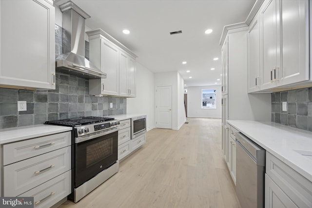 kitchen featuring light wood finished floors, light countertops, recessed lighting, appliances with stainless steel finishes, and wall chimney exhaust hood