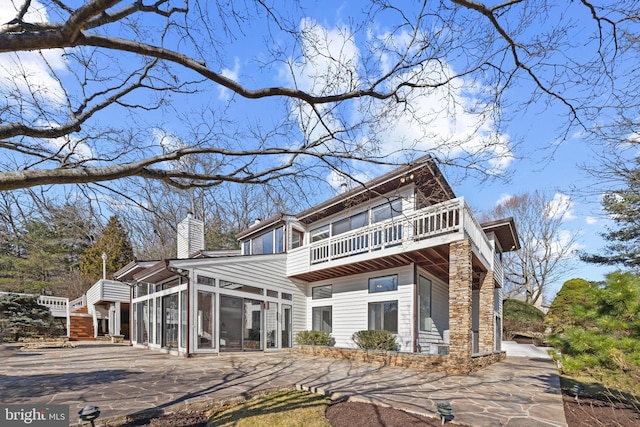 rear view of house with a balcony, a chimney, and a sunroom