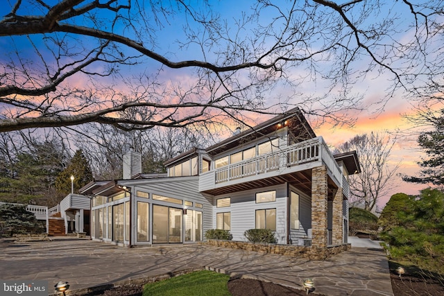 view of front of property featuring a chimney, a balcony, and a sunroom