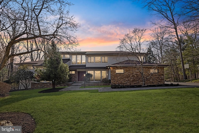 rear view of house with stone siding and a lawn