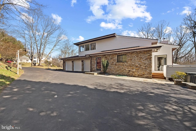 view of front of house featuring aphalt driveway, central AC unit, stone siding, and a chimney