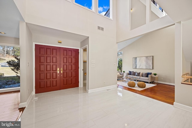 entrance foyer with visible vents, baseboards, a high ceiling, and wood finished floors