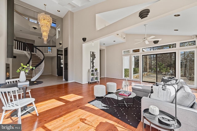 living room featuring baseboards, stairs, ceiling fan with notable chandelier, wood finished floors, and high vaulted ceiling