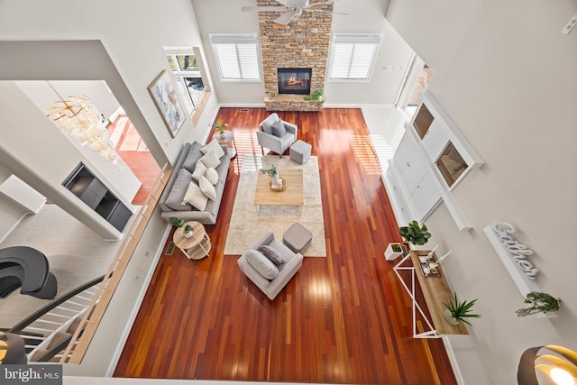 living area featuring a stone fireplace, wood finished floors, baseboards, and a ceiling fan