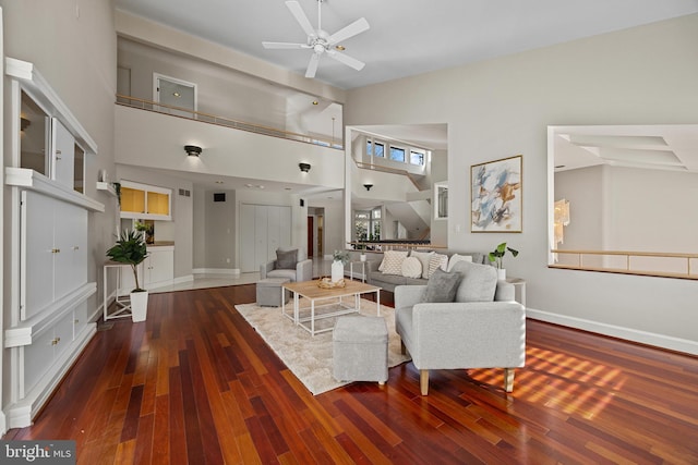 living room with baseboards, wood-type flooring, a high ceiling, and ceiling fan