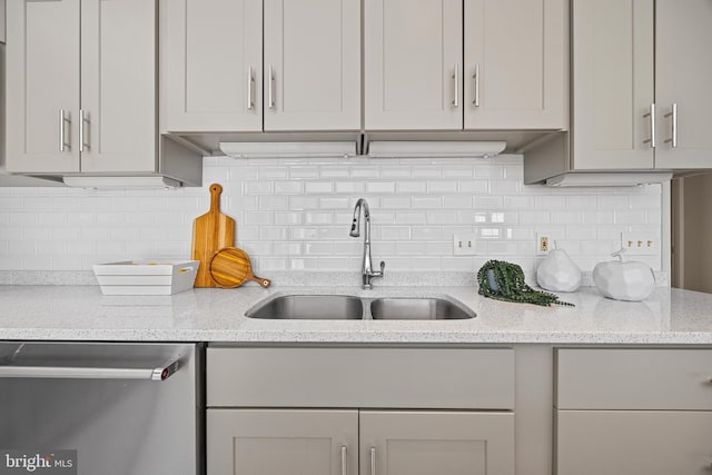 kitchen with stainless steel dishwasher, light stone counters, backsplash, and a sink