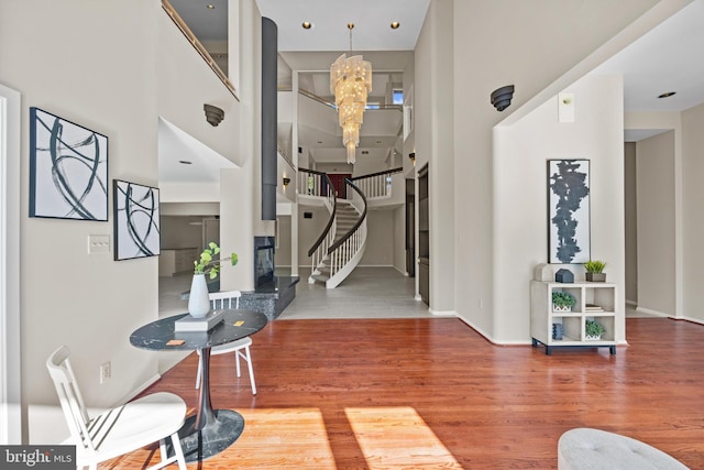 entryway with a notable chandelier, wood finished floors, baseboards, a towering ceiling, and stairs