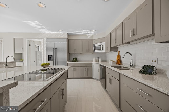 kitchen with a sink, stainless steel appliances, light stone countertops, and gray cabinets