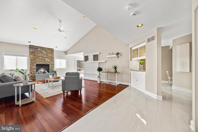 living room featuring a fireplace, high vaulted ceiling, baseboards, and wood finished floors