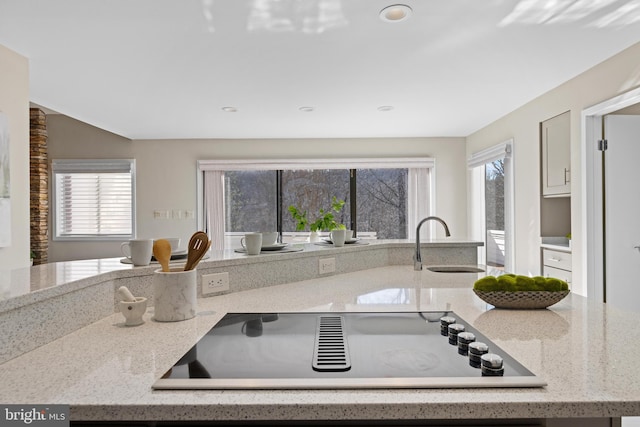 kitchen with a sink, black electric stovetop, and light stone countertops