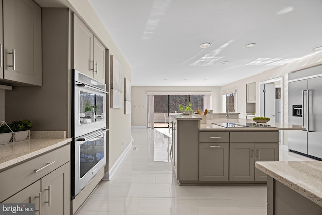 kitchen featuring light stone counters, appliances with stainless steel finishes, gray cabinetry, and an island with sink