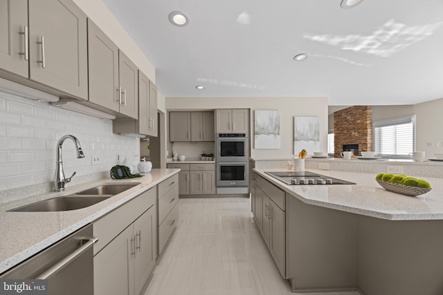 kitchen with a sink, light stone counters, appliances with stainless steel finishes, and gray cabinetry