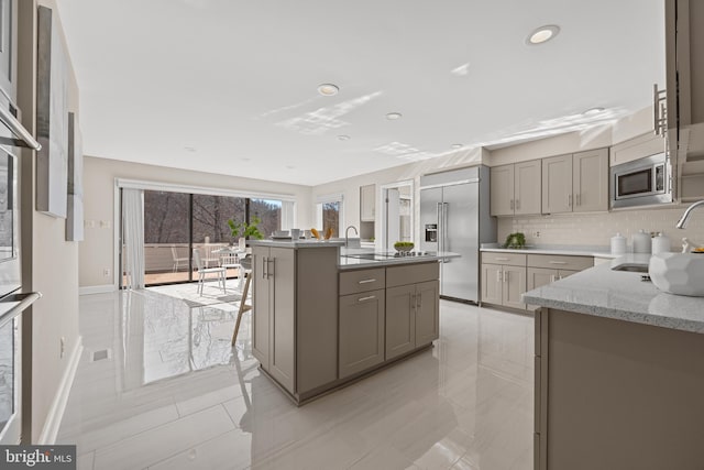 kitchen with a center island with sink, gray cabinets, a sink, tasteful backsplash, and built in appliances