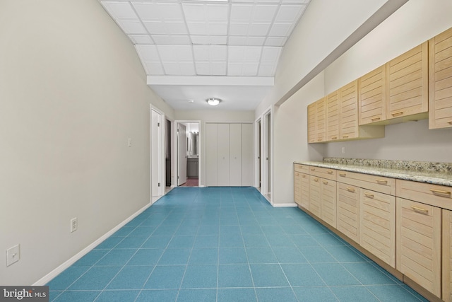 interior space with light brown cabinets, baseboards, dark tile patterned floors, a drop ceiling, and light countertops