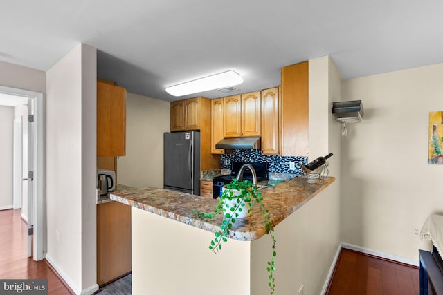 kitchen with under cabinet range hood, backsplash, wood finished floors, stainless steel appliances, and baseboards