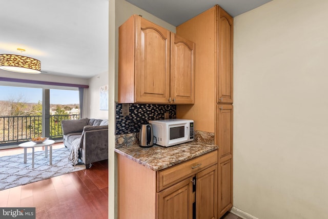 kitchen with white microwave, open floor plan, light stone counters, decorative backsplash, and wood finished floors