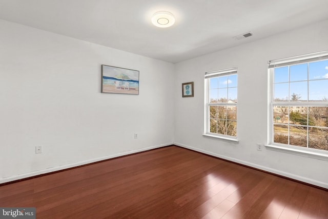 spare room featuring a wealth of natural light, visible vents, baseboards, and wood finished floors