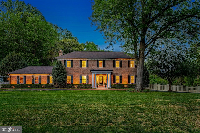 colonial home featuring brick siding, fence, a chimney, and a front lawn