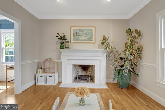 living room with crown molding, a fireplace with flush hearth, baseboards, and wood finished floors