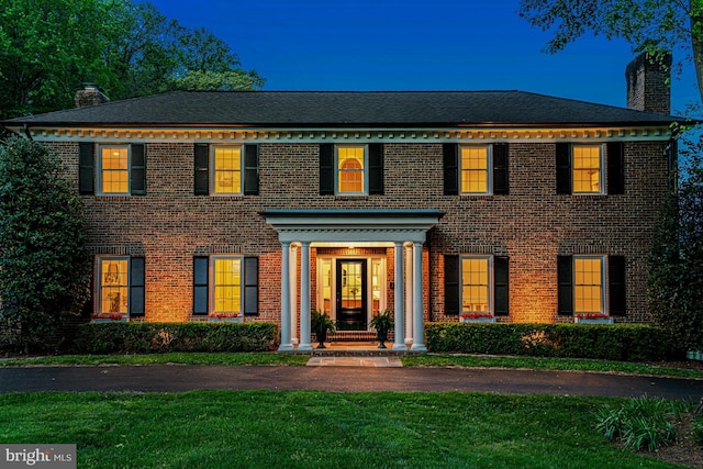 colonial inspired home featuring a chimney, a front lawn, and brick siding
