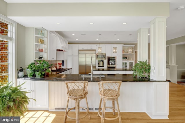 kitchen featuring decorative backsplash, open shelves, a peninsula, built in appliances, and light wood-style flooring