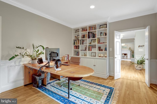 office with light wood-style floors, wainscoting, crown molding, and a decorative wall