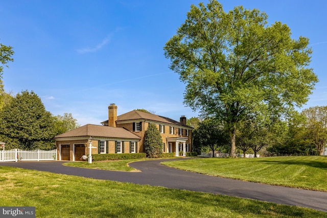 view of front of house with a front lawn, fence, a chimney, an attached garage, and driveway