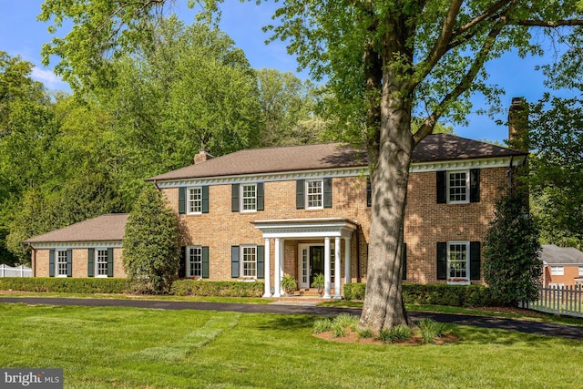 view of front of property featuring brick siding, fence, a chimney, and a front lawn