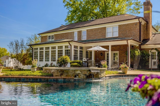 back of property with an outdoor pool, a chimney, a sunroom, brick siding, and a patio area