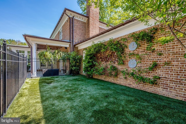 back of house with fence, a chimney, a yard, and brick siding