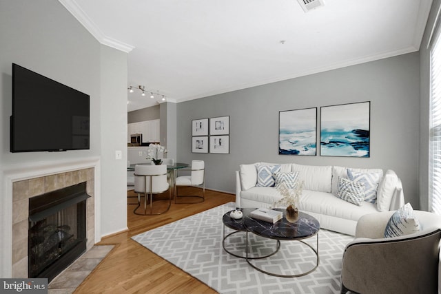 living area with wood finished floors, visible vents, a tile fireplace, track lighting, and crown molding