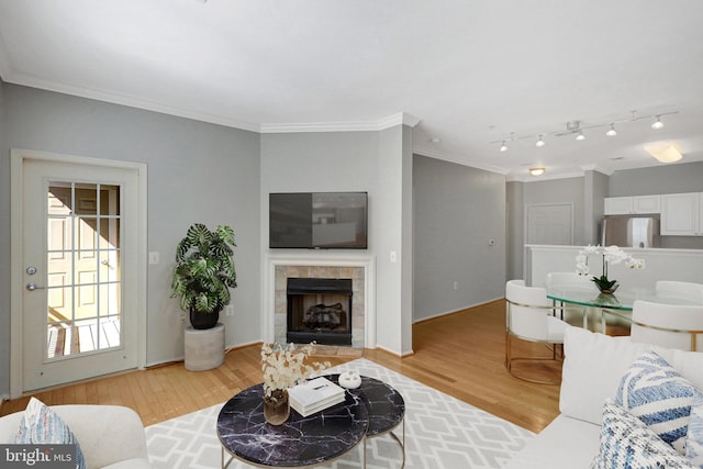 living area featuring light wood-type flooring, ornamental molding, and a tile fireplace