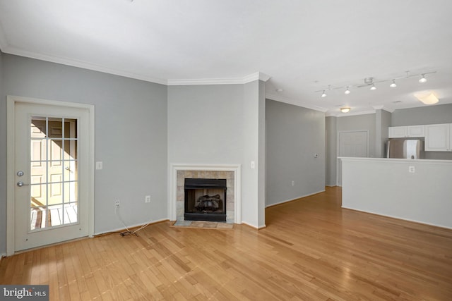 unfurnished living room featuring a tiled fireplace, crown molding, and light wood-type flooring