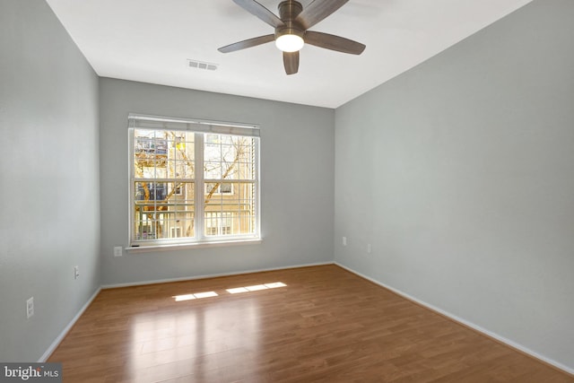 unfurnished room with a ceiling fan, wood finished floors, visible vents, and baseboards