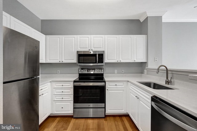 kitchen with light wood-style flooring, a sink, appliances with stainless steel finishes, white cabinets, and light countertops