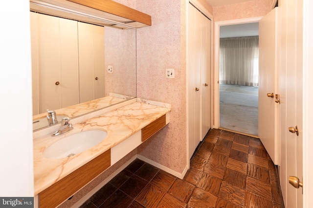 bathroom with baseboards, vanity, and wallpapered walls