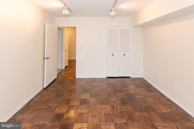 unfurnished bedroom with a closet, baseboards, and rail lighting