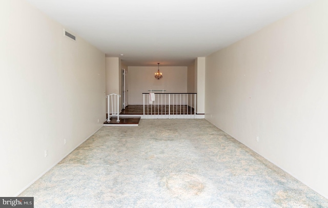 carpeted spare room featuring visible vents and a notable chandelier