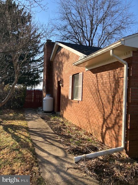 view of home's exterior with brick siding, a chimney, and fence