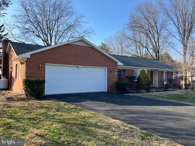 single story home featuring a chimney, brick siding, an attached garage, and driveway