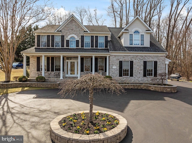 view of front facade featuring a porch, brick siding, roof with shingles, and aphalt driveway