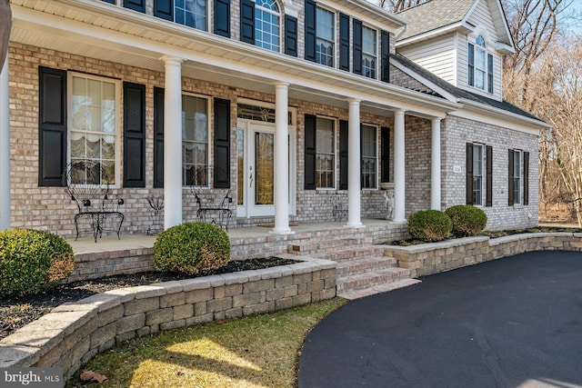 entrance to property featuring a porch and brick siding