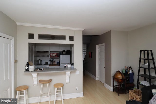 kitchen featuring light wood-type flooring, a breakfast bar, freestanding refrigerator, light countertops, and baseboards