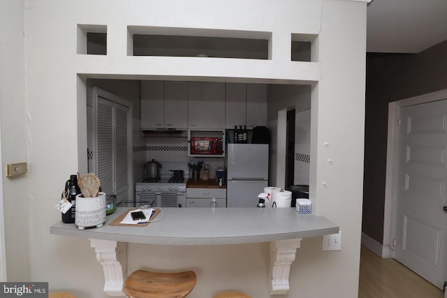 kitchen with white appliances, a breakfast bar, a peninsula, light countertops, and backsplash