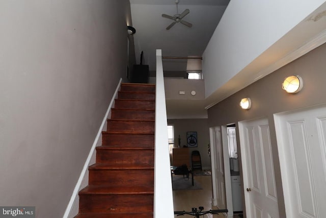 stairway featuring a high ceiling, a ceiling fan, and baseboards